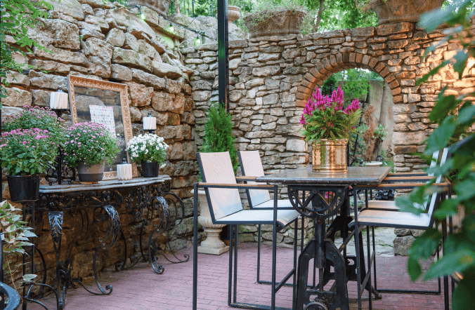Table and chairs on the brick courtyard beside a stone archway and potted flowers