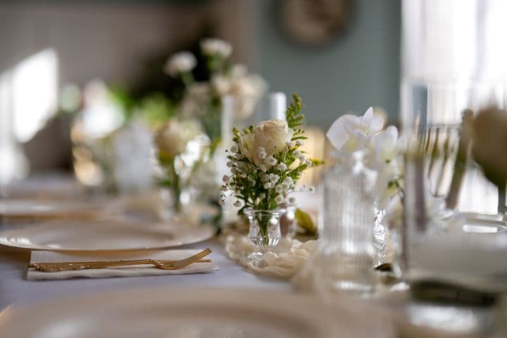 A white rose centerpiece on a table set for a wedding