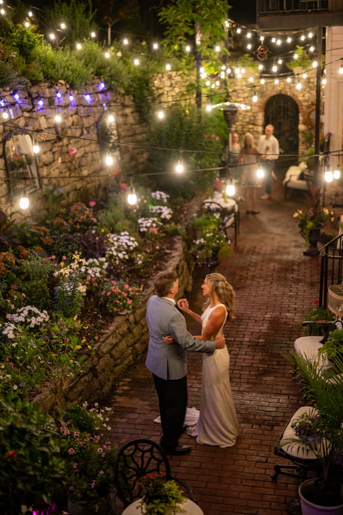 Newlyweds sharing a first dance in the garden courtyard under string lights